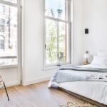 Helles Schlafzimmer mit Leinenbett und Rattansessel am Fenster