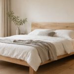 Niedriges Massivholzbett mit weißer Leinenbettwäsche in hellem Schlafzimmer
